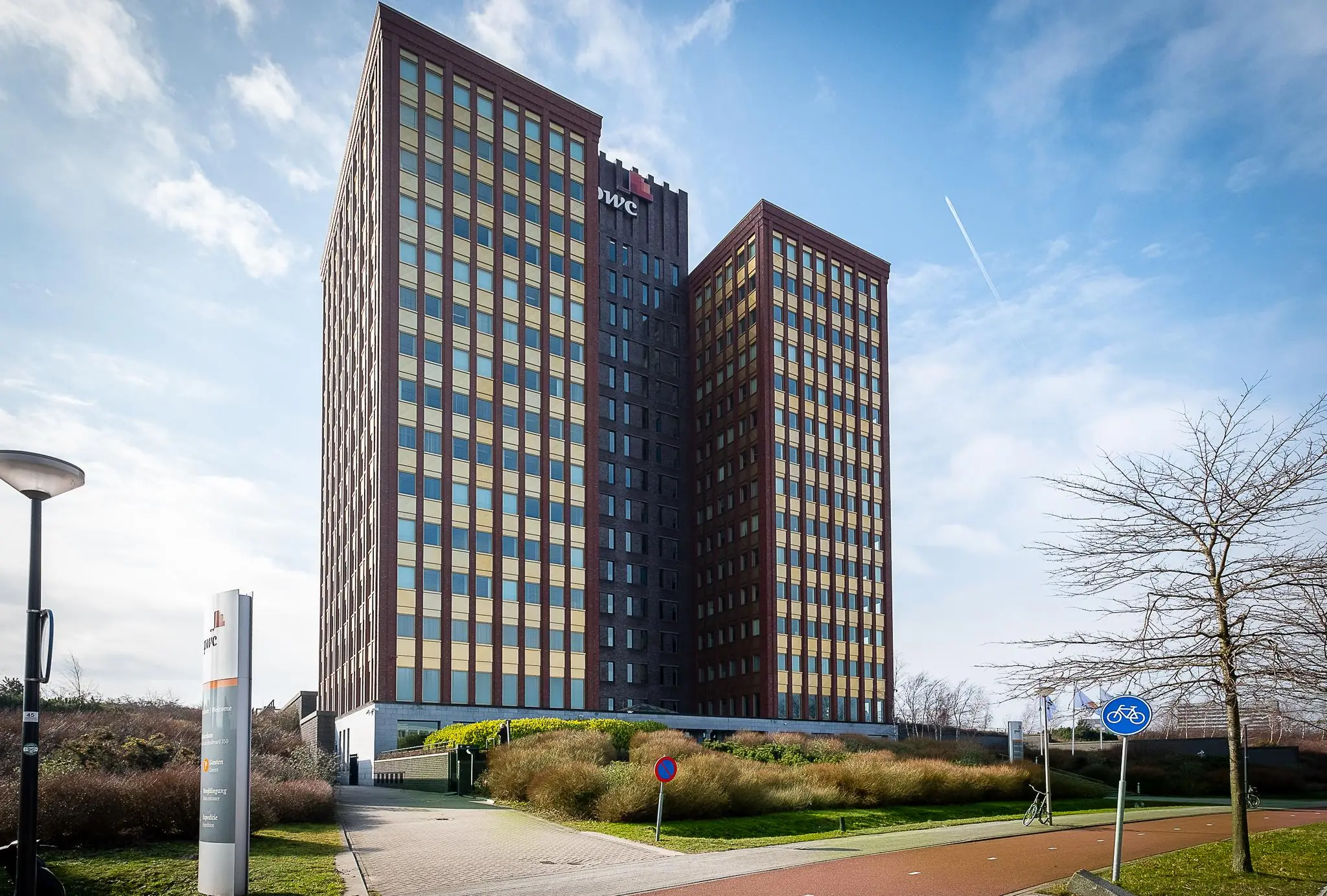 Hoog kantoorgebouw van PwC aan de Fascinatio Boulevard met groenvoorziening en fietspad op de voorgrond.